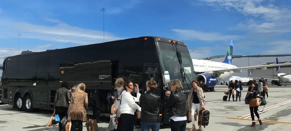 Group of travelers with luggage boarding a black motor coach at an airport