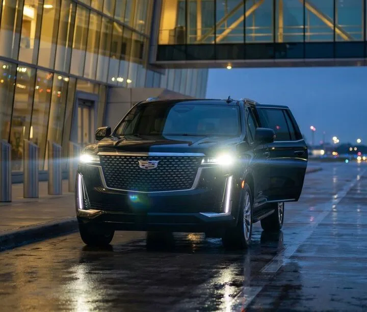Black Cadillac Escalade executive SUV with headlights on at an airport terminal at night