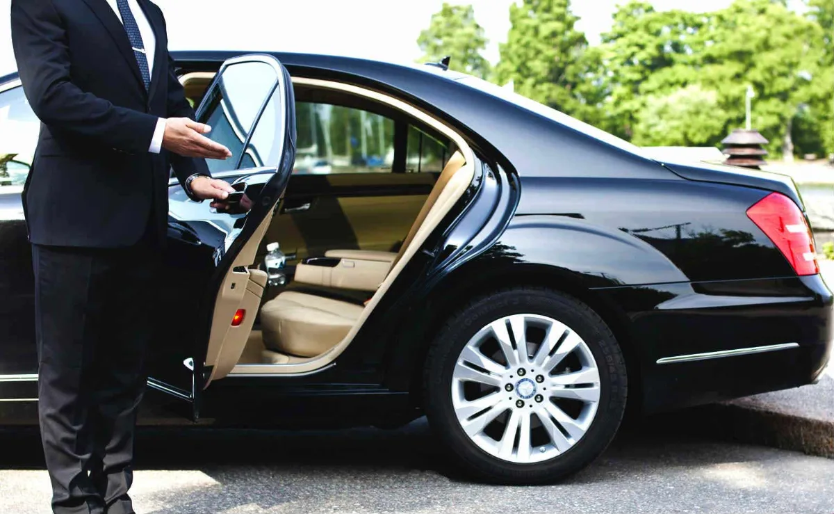 Chauffeur opening the rear door of a black Mercedes S-Class with a tan leather interior