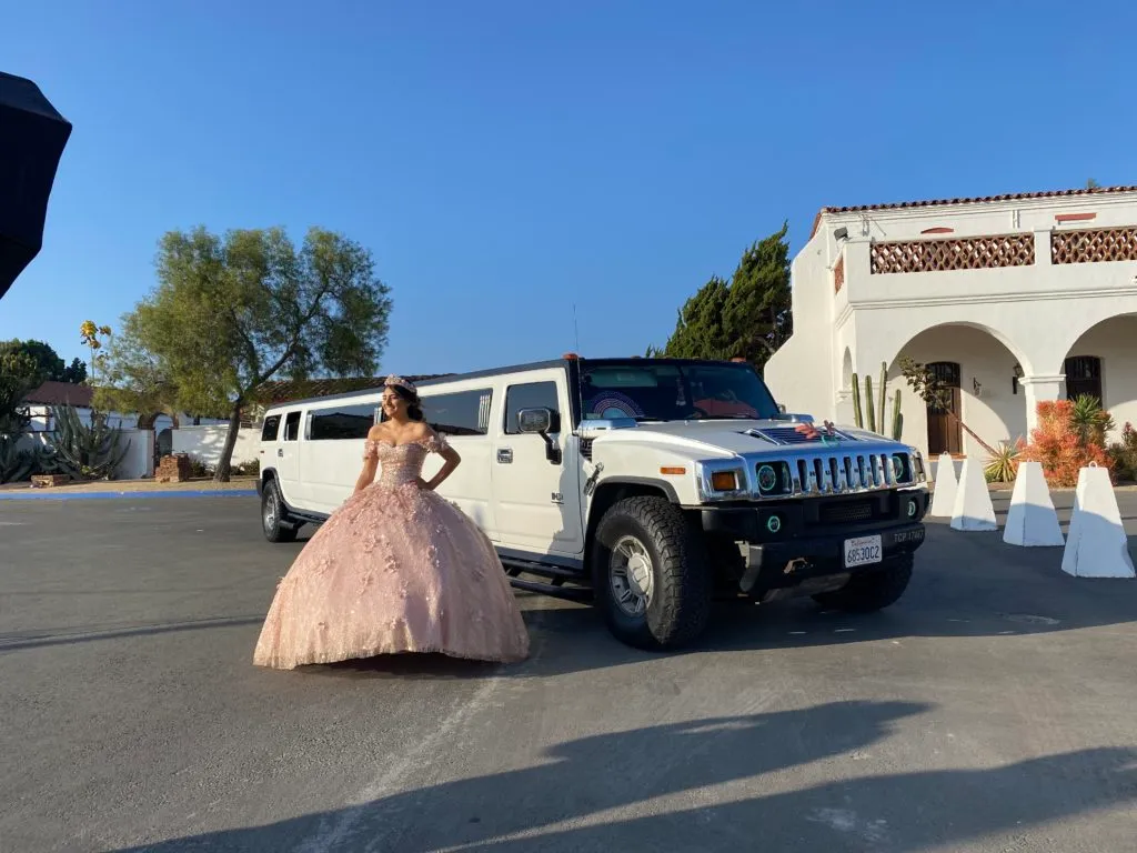White Hummer stretch limo with a quinceañera in a pink gown outside a venue