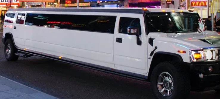 White Hummer stretch limousine side view on a city street at night